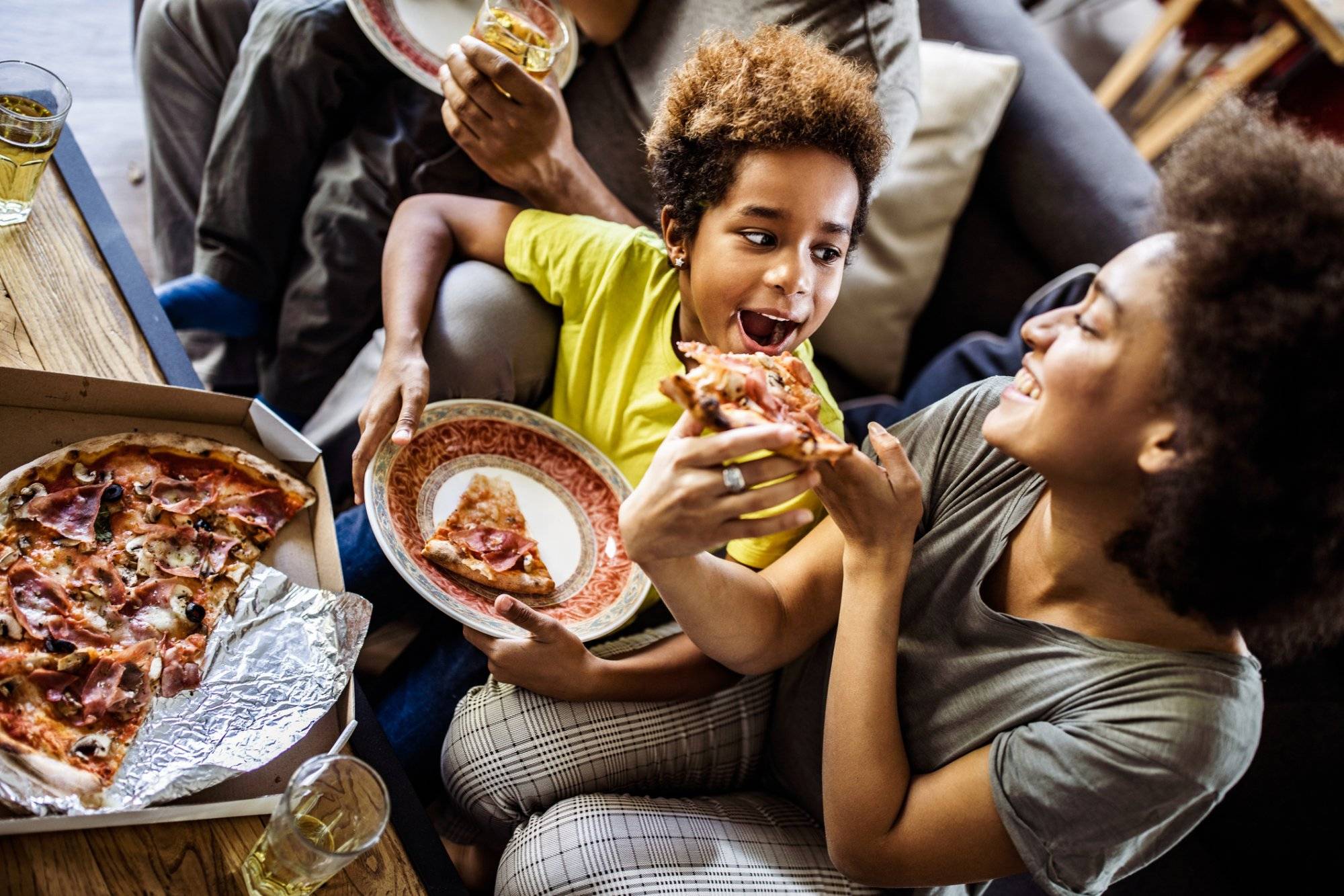 Above view of black mother feeding her daughter with pizza at home.