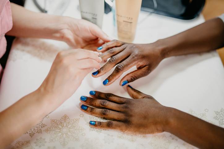 African ethnicity woman at spa receiving manicure from professional beautician